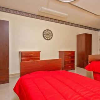 A tidy bedroom featuring twin beds with red bedding, wooden dressers, a wardrobe, and a wall clock.