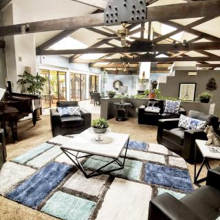 A spacious and modern living room featuring exposed wooden beams, a grand piano, and stylish furniture.