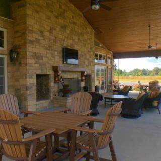 A cozy outdoor patio with a stone fireplace, wooden furniture, and a television.