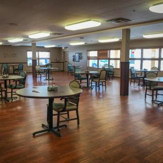 An empty dining room with several round tables and chairs, featuring a wooden floor and large windows.