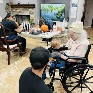 A family gathering where an elderly woman in a wheelchair interacts with a child in a cozy living room adorned with autumn decorations.