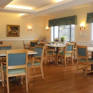 A cozy dining area with several tables and chairs, featuring wooden flooring and natural lighting from the windows.