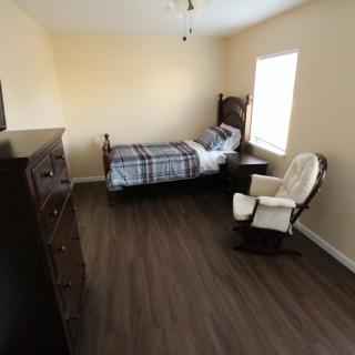 A simple bedroom with a single bed, dresser, and rocking chair.