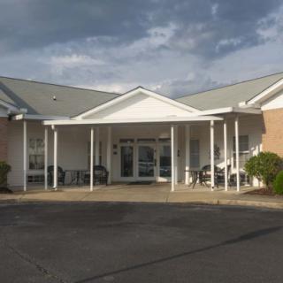 A building with a covered entrance and white columns under a cloudy sky.