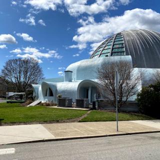 A striking modern architectural structure surrounded by greenery and under a bright sky.