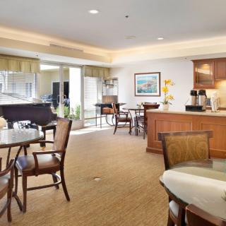 A cozy dining area with tables, chairs, a piano, and a coffee station under bright lighting.
