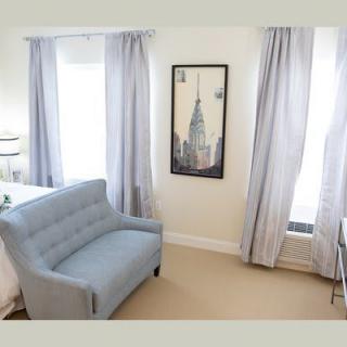 A cozy living room featuring a blue sofa, light curtains, and artwork on the wall.