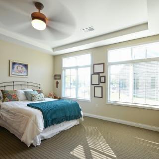 A bright and cozy bedroom with large windows, a ceiling fan, and stylish decor.