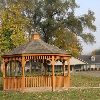 A wooden gazebo in a park surrounded by autumn trees.