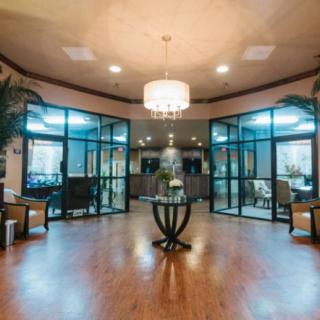 A modern lobby with a chandelier, glass doors, and a central table surrounded by seating.
