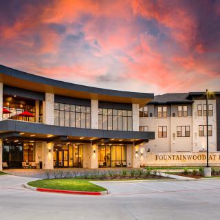 A modern building with a curved entrance under a vibrant sunset sky.
