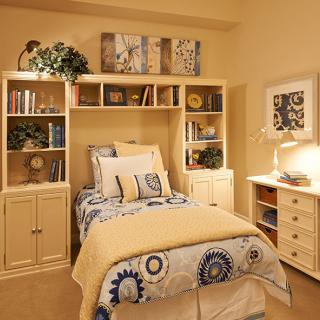 A cozy bedroom with a single bed, bookshelf, and warm lighting.