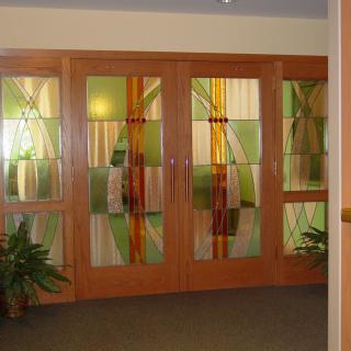 A set of stained glass doors with a wooden frame, decorated with plants on either side.