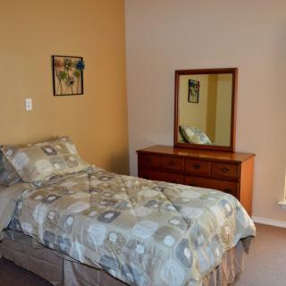 A cozy bedroom with a single bed and a wooden dresser topped with a mirror.
