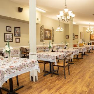 A spacious and elegantly decorated dining area in a restaurant, featuring tables set with floral tablecloths under charming chandeliers.