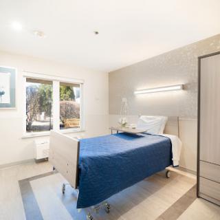 A modern hospital patient room featuring a neatly made bed with a blue blanket and large windows providing natural light.