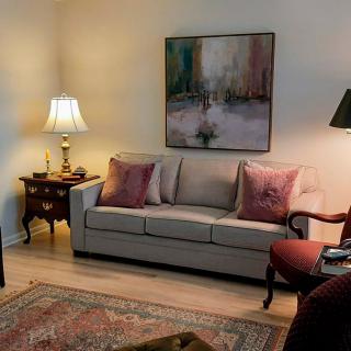 A cozy living room featuring a comfortable sofa with cushions, an elegant lamp on a side table, and abstract artwork on the wall.