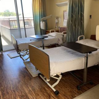 A hospital room with two neatly arranged beds, featuring medical equipment and privacy curtains.