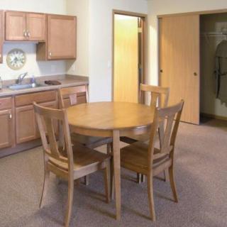 A cozy kitchen and dining area with a wooden table and four chairs, complete with wooden cabinets and carpeted flooring.