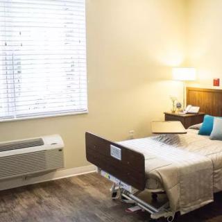 A cozy hospital room with a single bed, lamp, and window providing natural light.