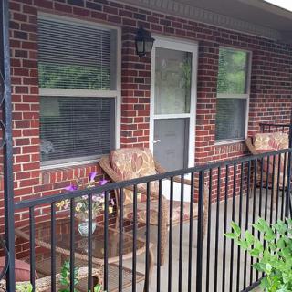 A cozy porch with two cushioned chairs, a brick wall, and a black metal railing.