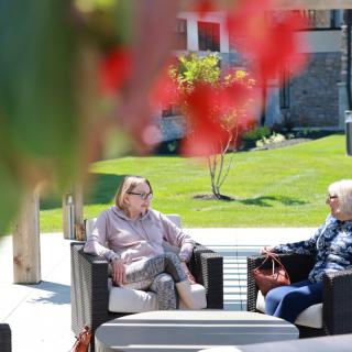 Two people engaging in conversation while seated outdoors on a sunny day.