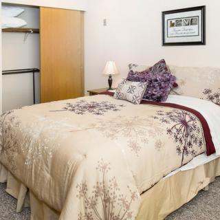 A cozy bedroom with a neatly made bed, decorative pillows, and an open closet.