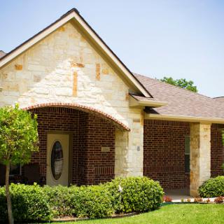 A charming residential house with a blend of brick and stone architecture, featuring well-maintained landscaping.