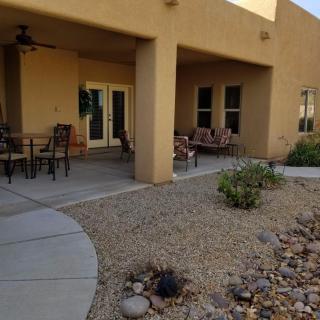 A cozy patio with outdoor seating and desert landscaping, featuring a covered area for shade.