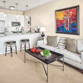 A modern living room with a neutral color palette, featuring a comfortable sofa, coffee table, and an open kitchen area adorned with contemporary artwork.