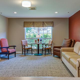 A cozy living room with a sofa, chairs, and a table near a bright window.