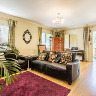 A cozy living room featuring a black leather sofa and armchair, a purple rug, wooden flooring, and decorative elements like a mirror and plants.