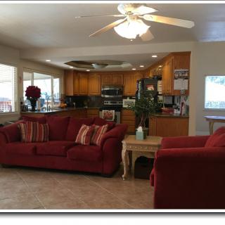 A cozy living room with red sofas, an adjacent kitchen with wooden cabinets, and a ceiling fan overhead.