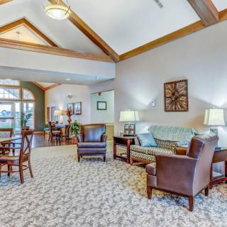 A spacious living room featuring comfortable seating, including a sofa and leather chairs, with decorative ceiling beams and warm lighting.