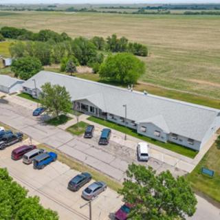 Aerial view of a building surrounded by fields and a parking lot with several cars.