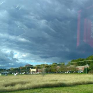 A dramatic sky with dark clouds looms over a grassy field and nearby buildings.