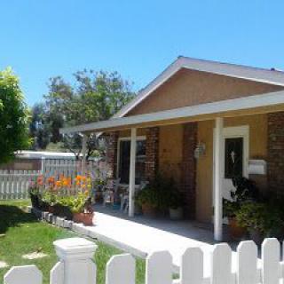A charming house with a front porch and garden, surrounded by a white picket fence on a sunny day.