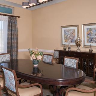 A well-decorated dining room featuring a polished wooden table surrounded by upholstered chairs, adorned with artwork and a vase of flowers.