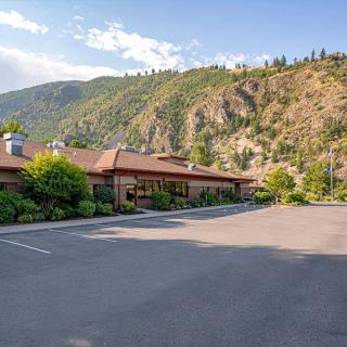 A single-story building with a red roof surrounded by a parking lot and scenic mountains.