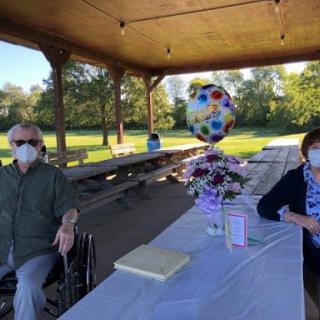 A small outdoor gathering with masked individuals enjoying a celebration under a picnic pavilion.
