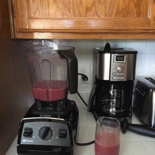 A kitchen countertop with a blender making a smoothie next to a coffee maker.