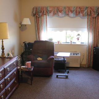 A cozy living room with an armchair, dresser, and window with curtains.