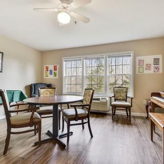 A cozy living room with a dining table set, piano, and large windows.