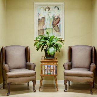 A cozy waiting area featuring two armchairs, a potted plant on a side table, and artwork on the wall.