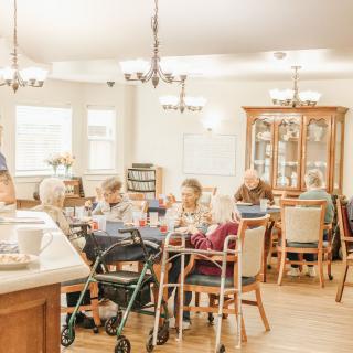 A group of elderly individuals in a nursing home dining area, engaging in conversation.