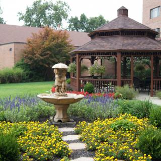 A tranquil garden scene featuring a fountain and gazebo surrounded by colorful flowers.