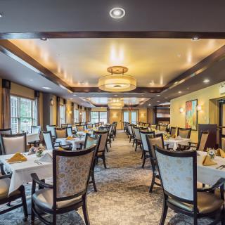 An elegantly decorated restaurant dining room with neatly arranged tables and chairs illuminated by stylish overhead lighting.