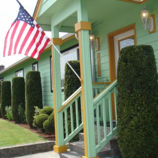 A green house with a porch and an American flag displayed, surrounded by neatly trimmed bushes.