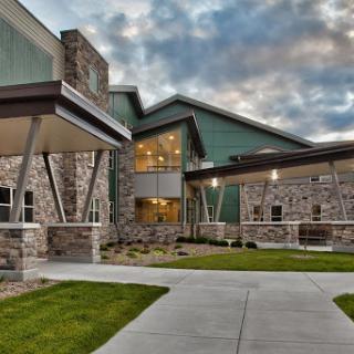 A modern stone and green building with a welcoming entrance surrounded by landscaped lawns.