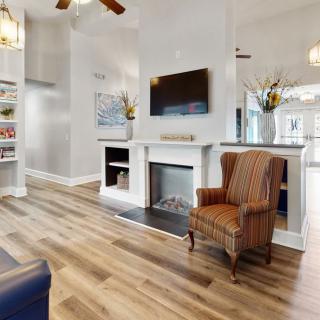 A modern living room with hardwood flooring, featuring a fireplace, mounted television, and a cozy armchair.